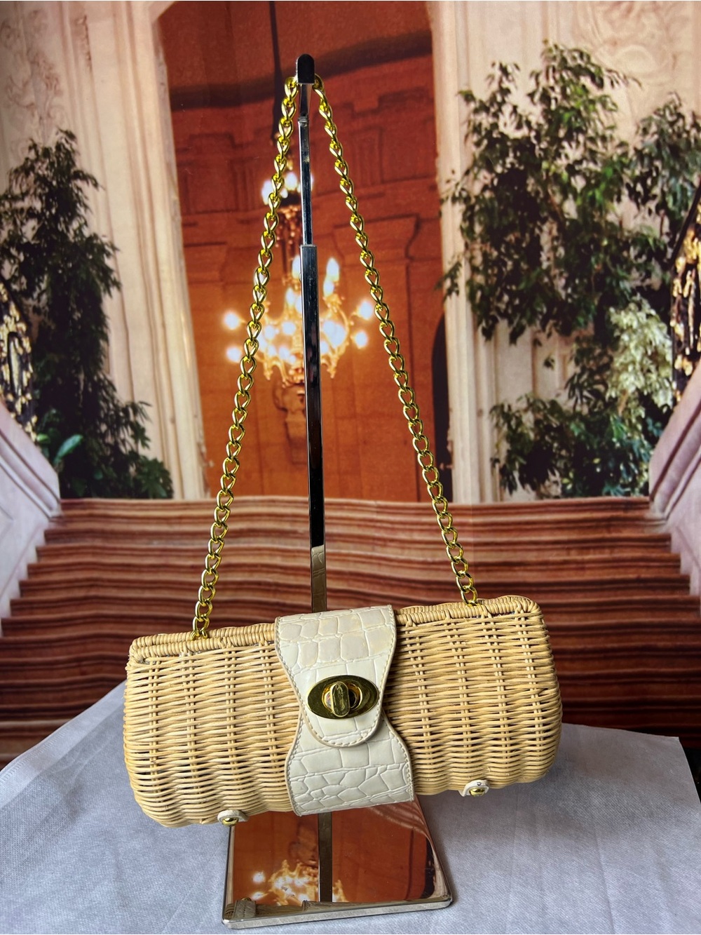 Wicker clutch features a textured cream faux leather closure & gold chain strap